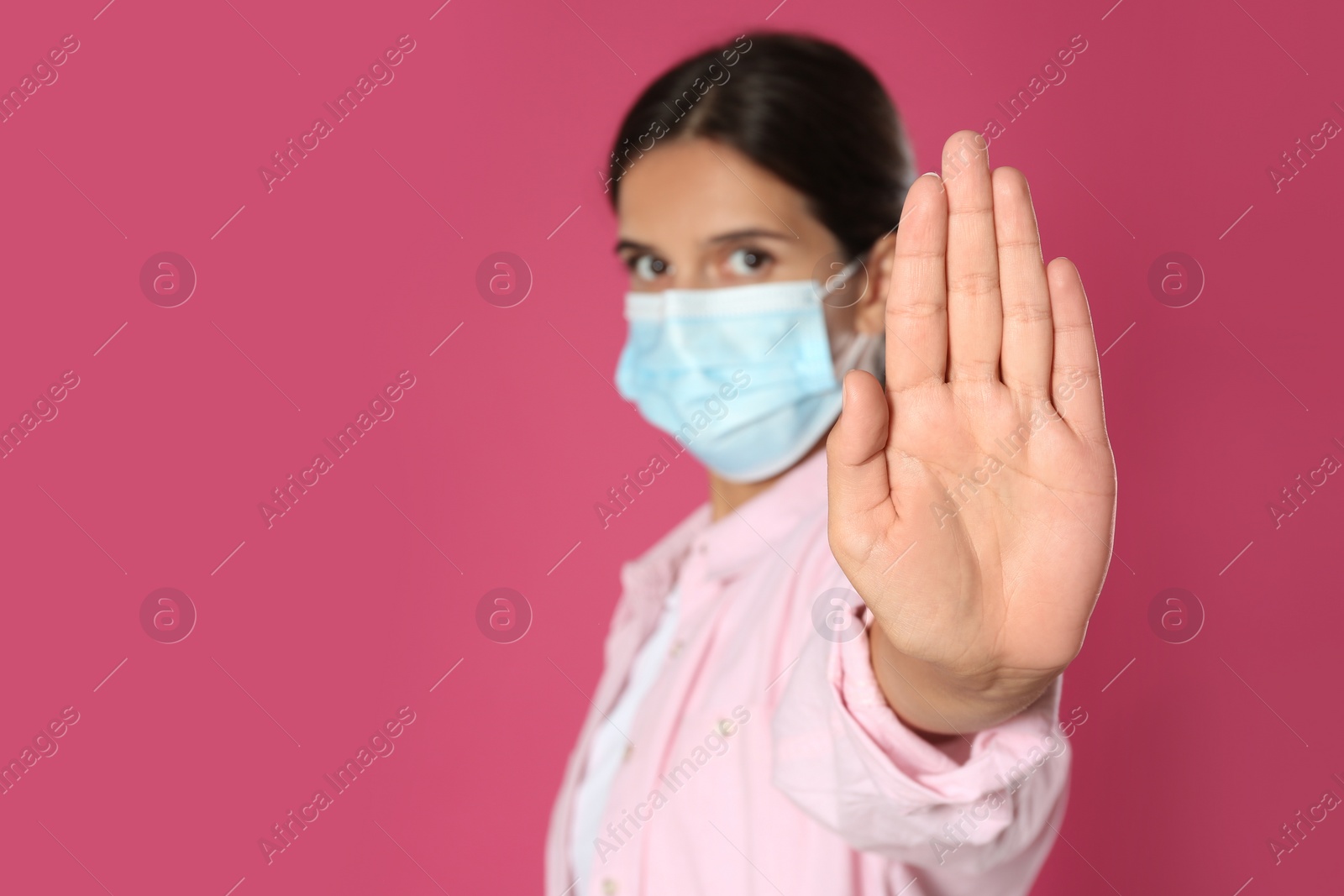 Photo of Woman in protective mask showing stop gesture on pink background, space for text. Prevent spreading of coronavirus