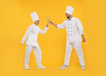 Photo of Happy professional confectioners in uniforms having fun on yellow background