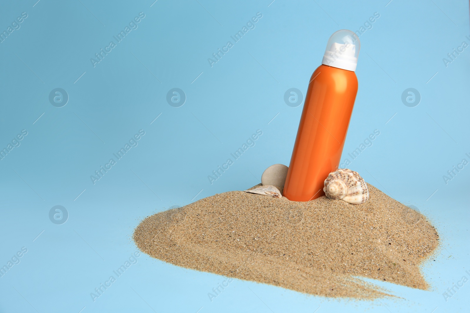 Photo of Sand with bottle of sunscreen, stone and seashell against light blue background, space for text. Sun protection