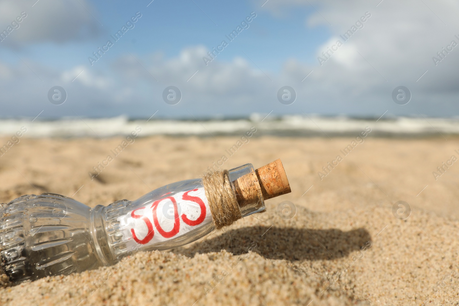 Photo of Glass bottle with SOS message on sand near sea, closeup