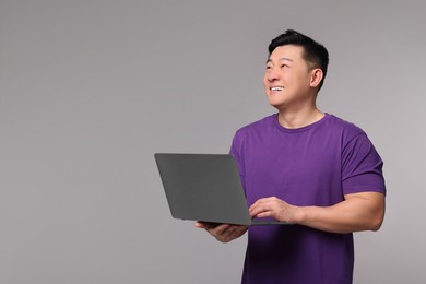 Happy man with laptop on grey background, space for text