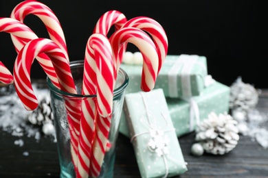 Many sweet Christmas candy canes and gift boxes on black wooden table. Space for text