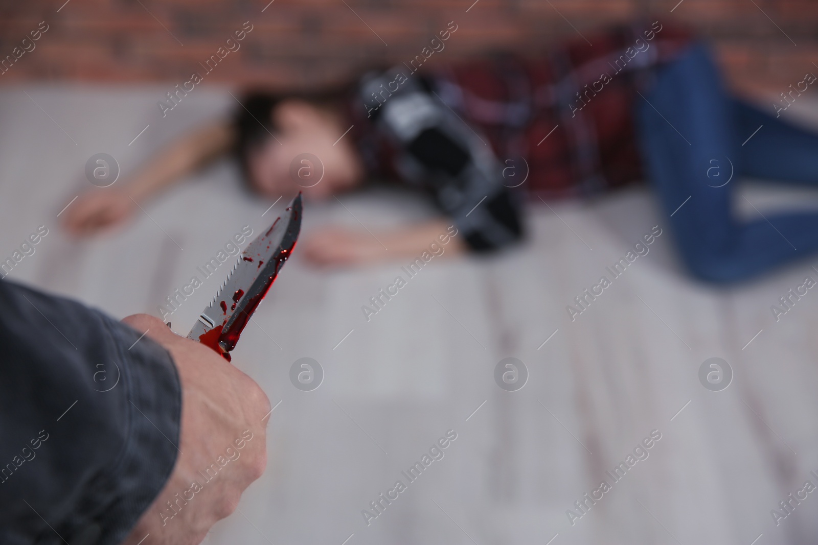 Photo of Man with bloody knife and his victim on floor indoors, closeup. Dangerous criminal