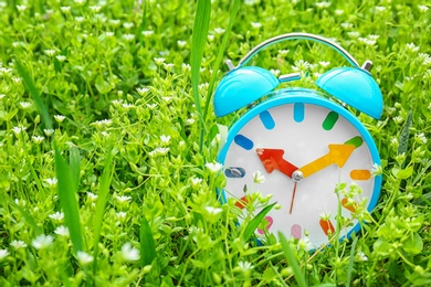 Photo of Alarm clock among flowers, outdoors. Time change concept