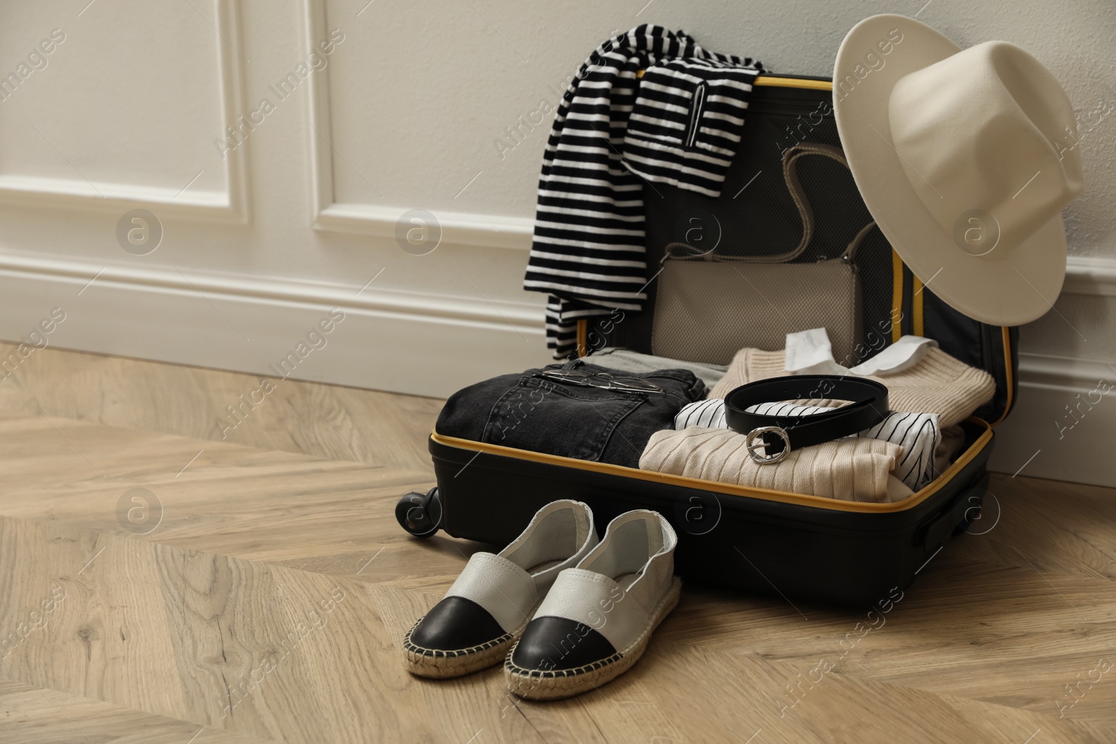 Photo of Open suitcase with folded clothes, accessories and shoes near white wall indoors, space for text