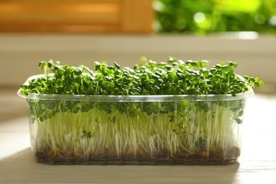 Photo of Sprouted arugula seeds in plastic container on white wooden table