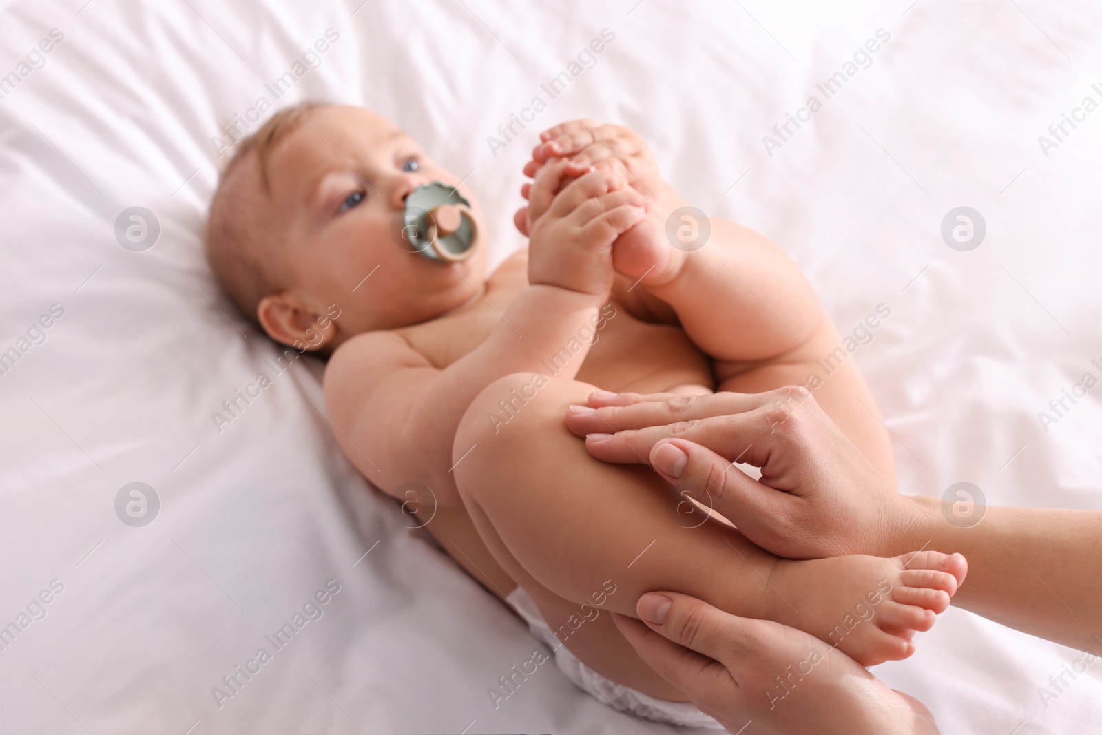 Photo of Mother massaging her cute baby with oil on bed, closeup