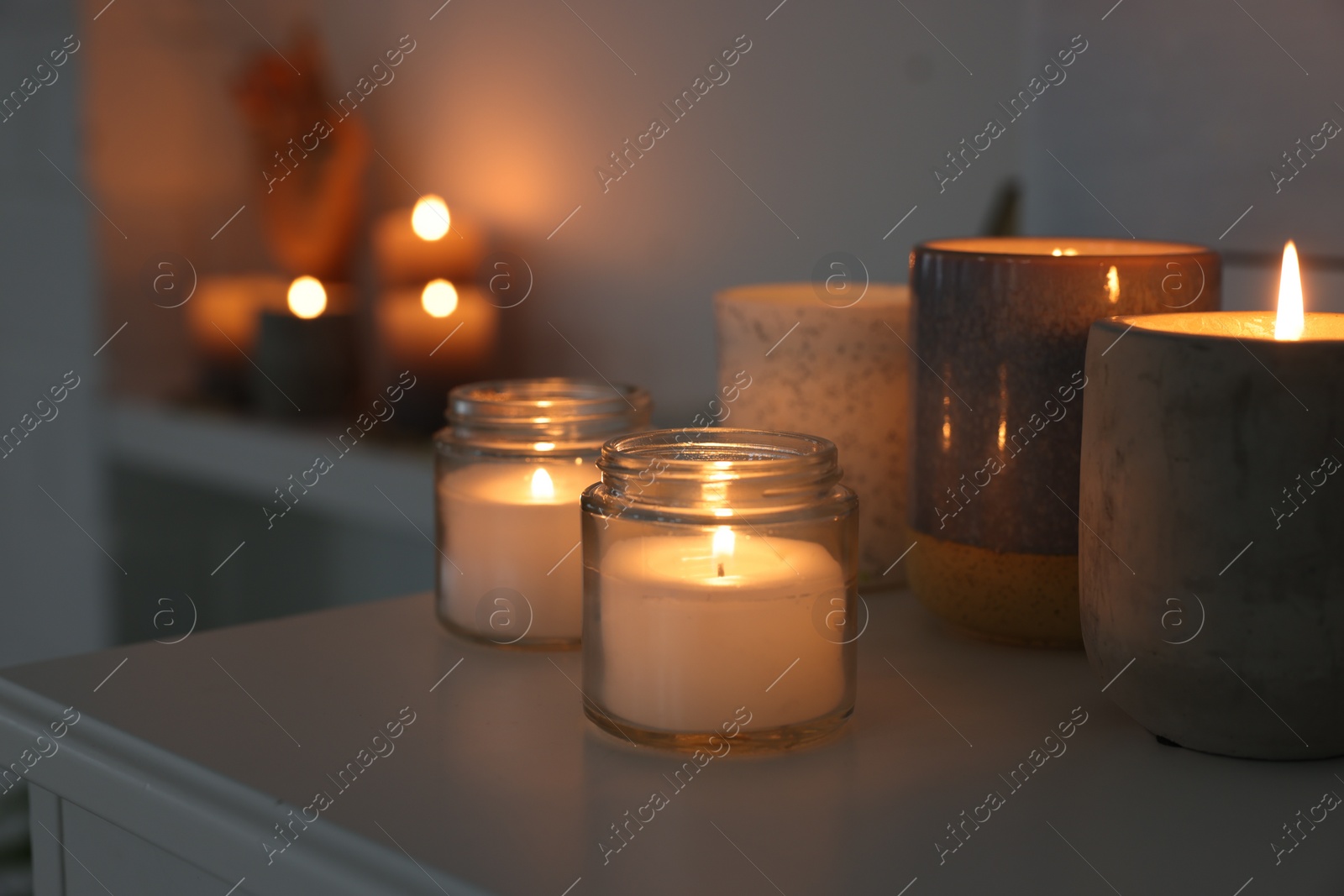 Photo of Burning wax candles on white table in room, space for text