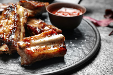 Photo of Board with delicious ribs on grey table, closeup