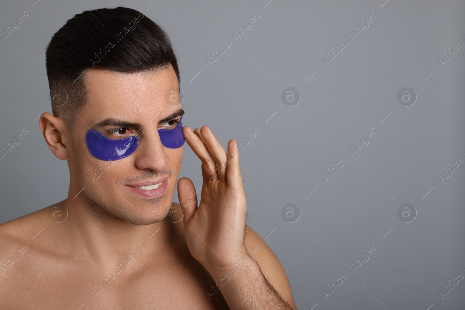 Photo of Man applying blue under eye patch on grey background. Space for text