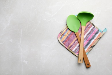 Different kitchen utensils and potholder on grey background, top view with space for text