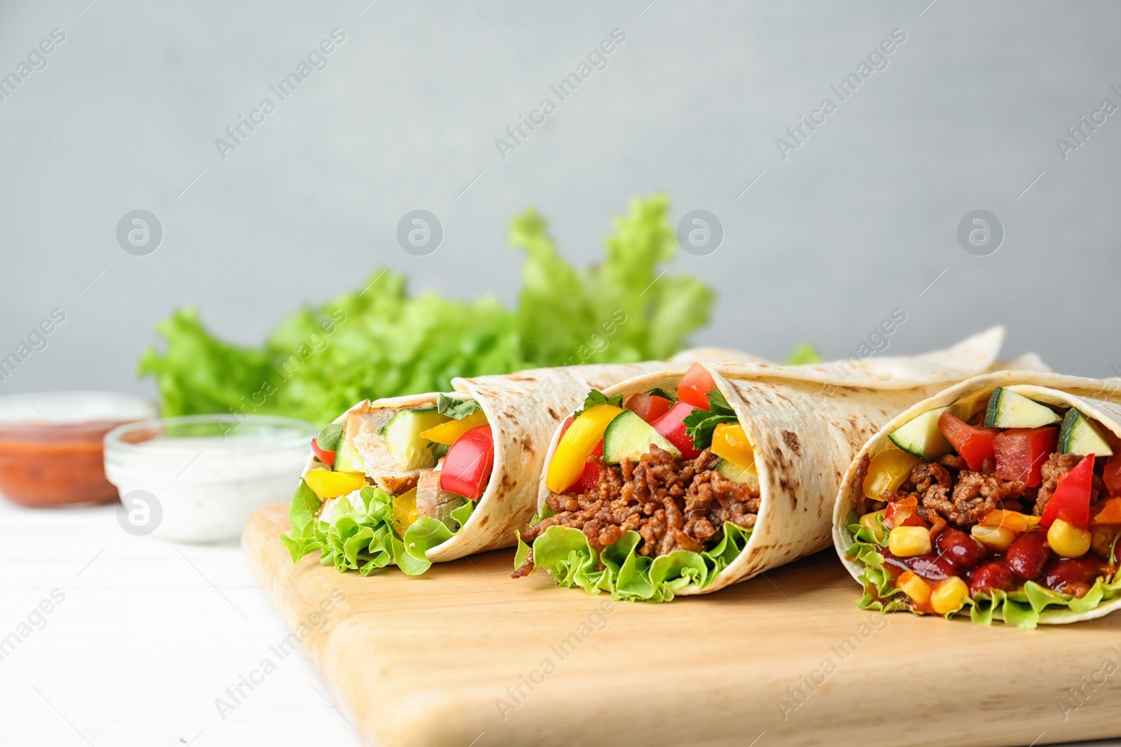 Photo of Delicious meat tortilla wraps on white wooden table against grey background