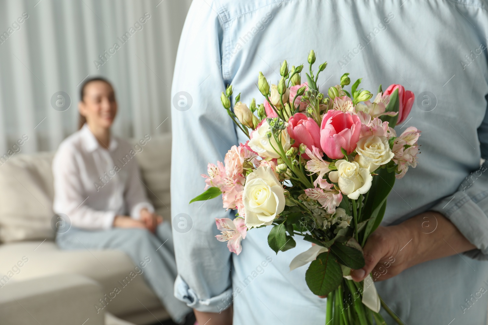 Photo of Man hiding bouquet of flowers for his beloved woman indoors, closeup