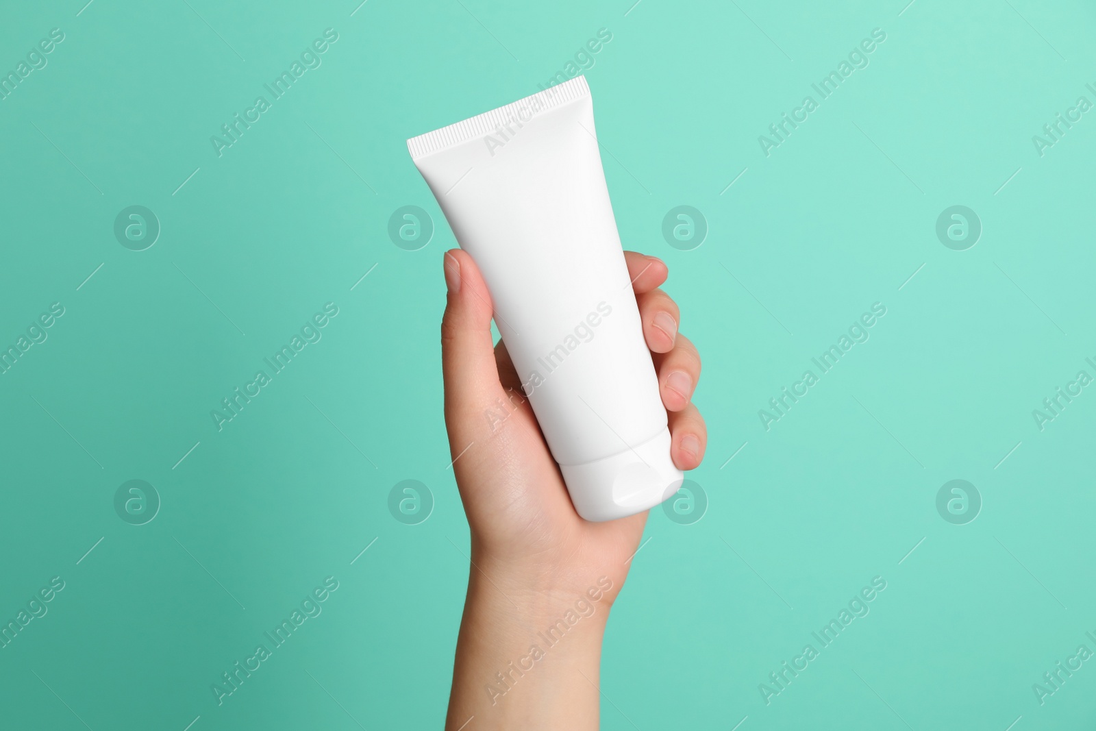 Photo of Woman holding tube of face cream on turquoise background, closeup