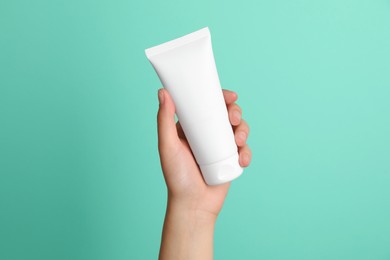 Photo of Woman holding tube of face cream on turquoise background, closeup
