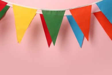 Photo of Buntings with colorful triangular flags hanging on pink background. Festive decor