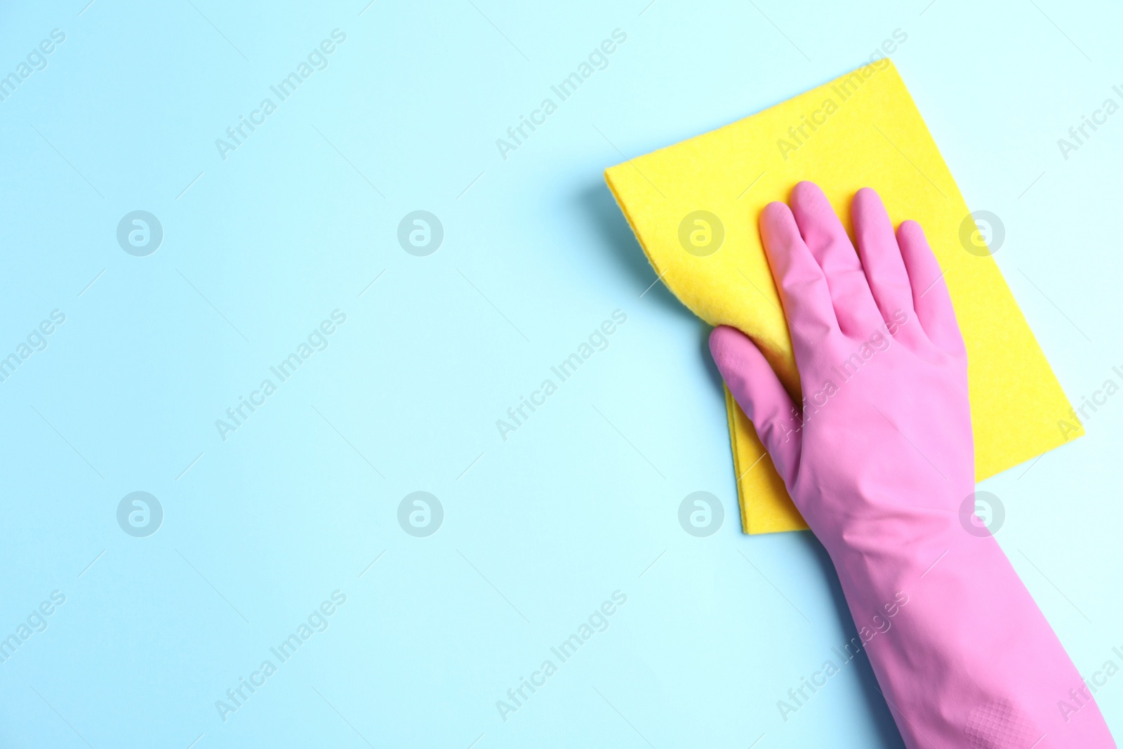 Photo of Person in rubber glove with rag on light blue background, closeup of hand. Space for text