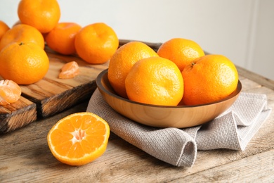 Photo of Bowl and board with ripe tangerines on wooden table