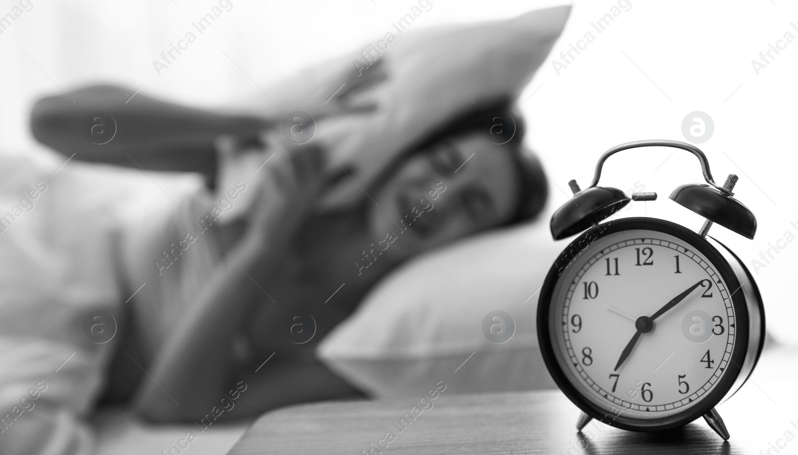 Image of Young woman covering ears with pillow at home in morning, selective focus. Black and white photography