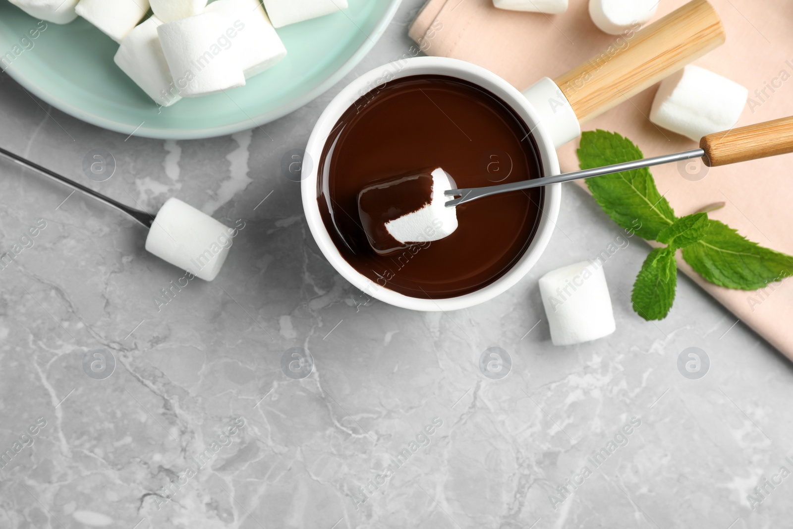 Photo of Dipping marshmallow into fondue pot with dark chocolate on marble table, top view