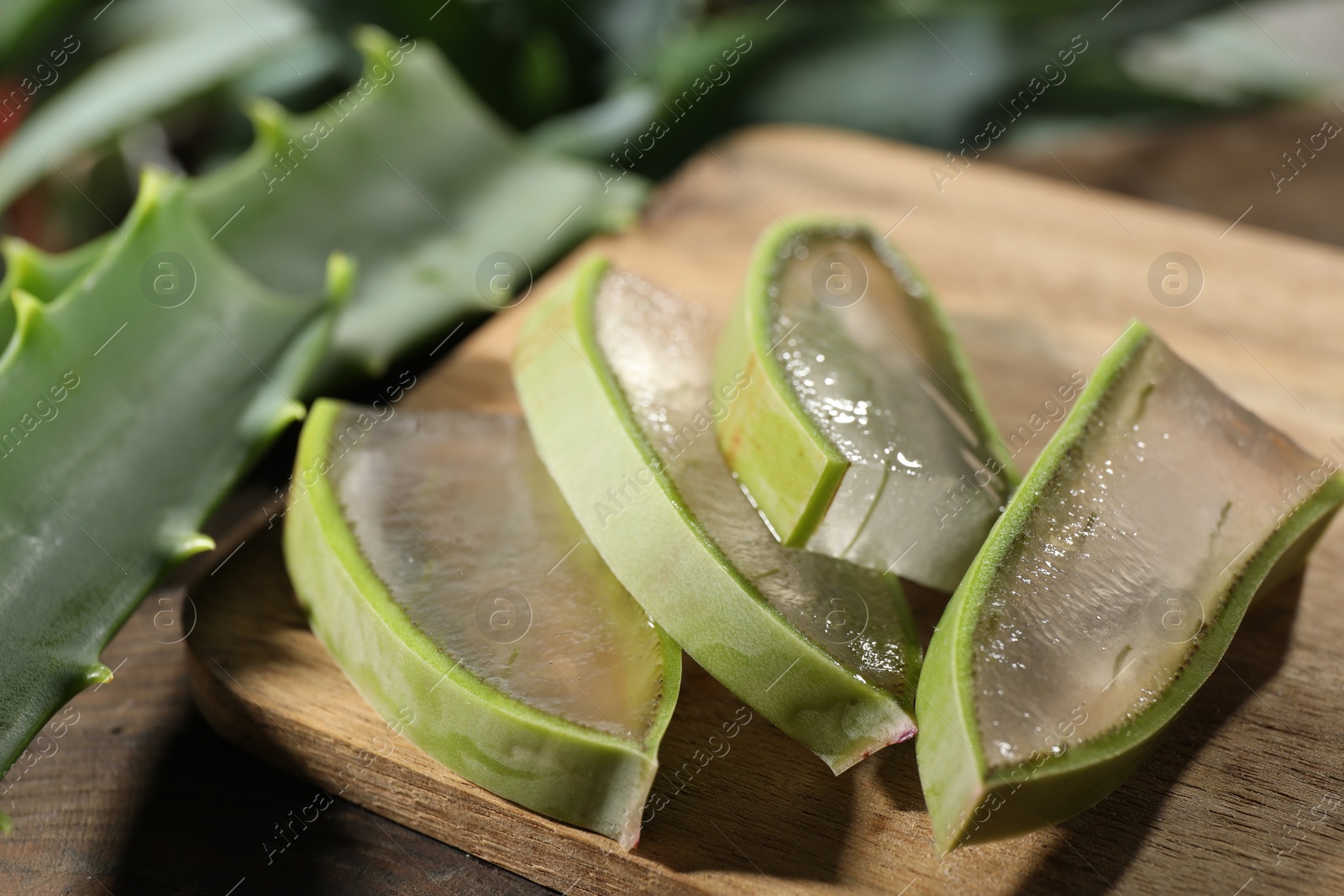 Photo of Slices of fresh aloe vera leaves with gel on wooden table, closeup