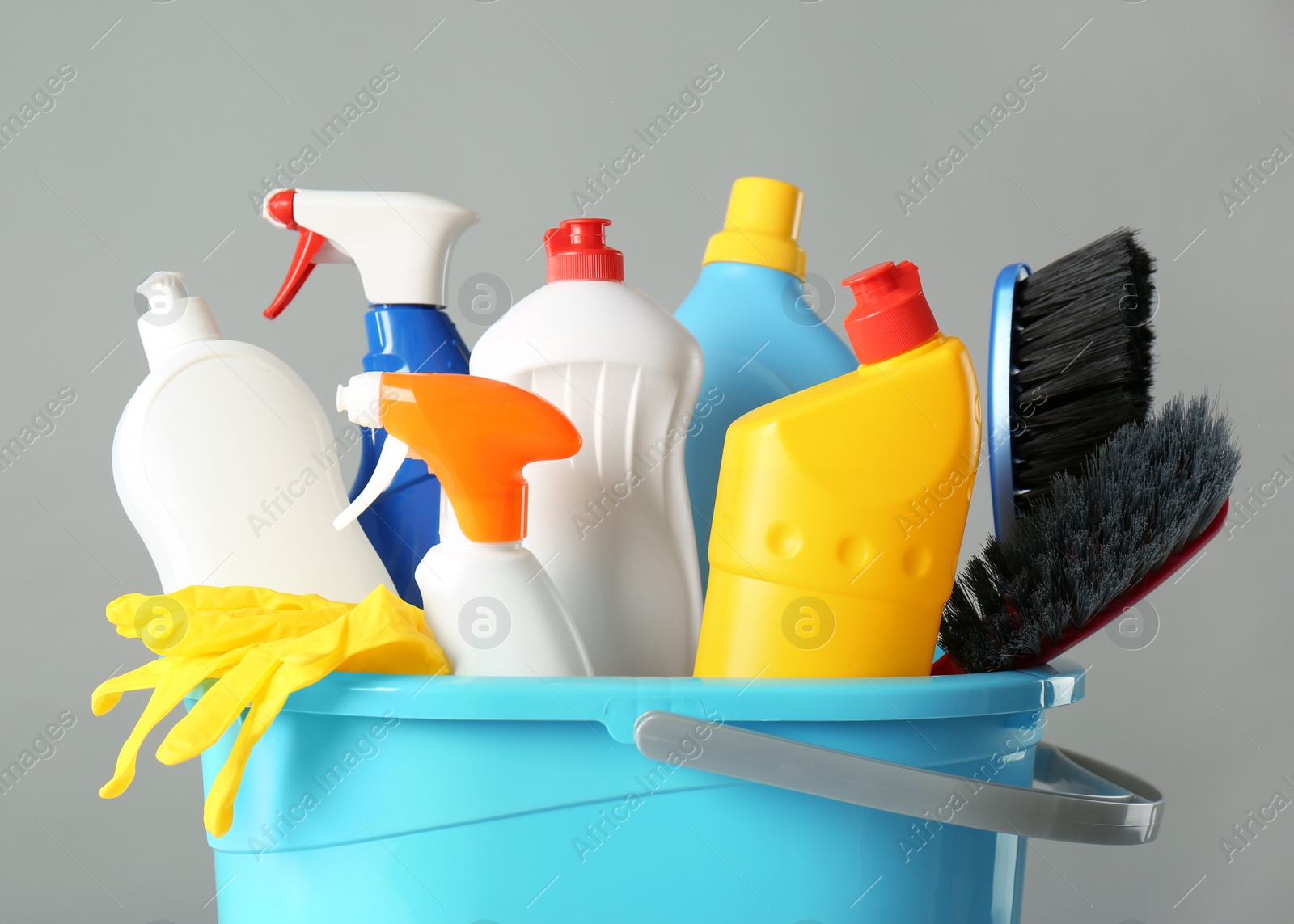 Photo of Bucket with cleaning products and tools on grey background, closeup