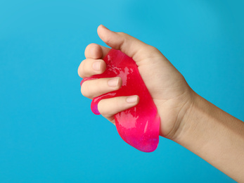 Photo of Woman playing with pink slime on light blue background, closeup. Antistress toy