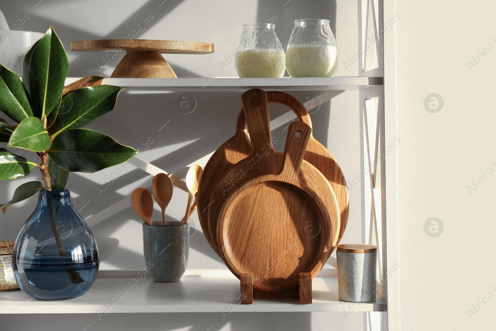 Photo of Wooden cutting boards, utensils, branch with green leaves and decor on shelving unit