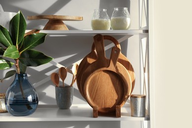 Wooden cutting boards, utensils, branch with green leaves and decor on shelving unit