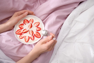 Photo of Young woman eating tasty yogurt with strawberries in bed