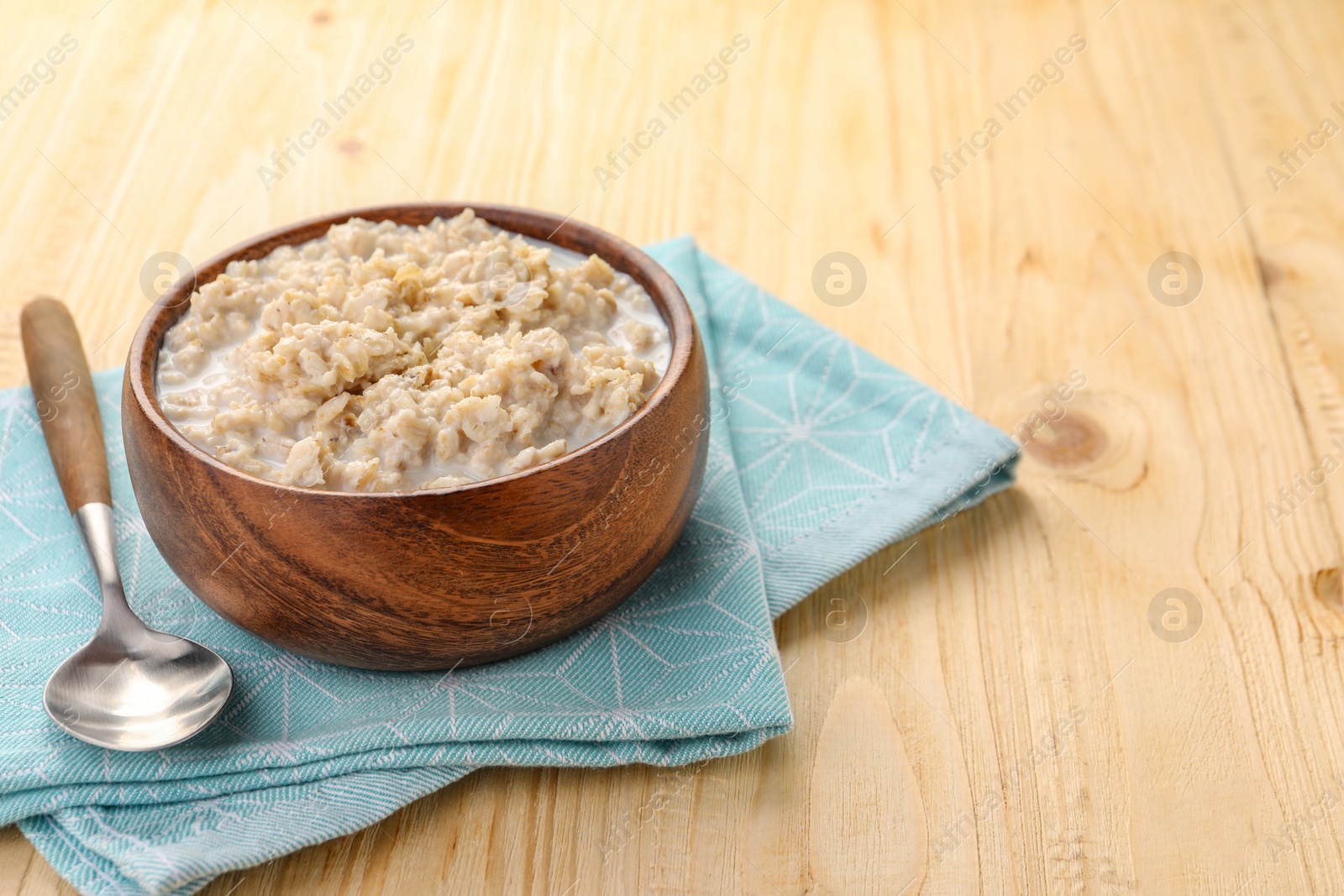 Photo of Tasty boiled oatmeal in bowl and spoon on wooden table, space for text