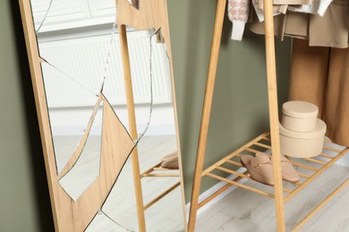 Broken mirror and wooden rack with clothes near olive wall indoors