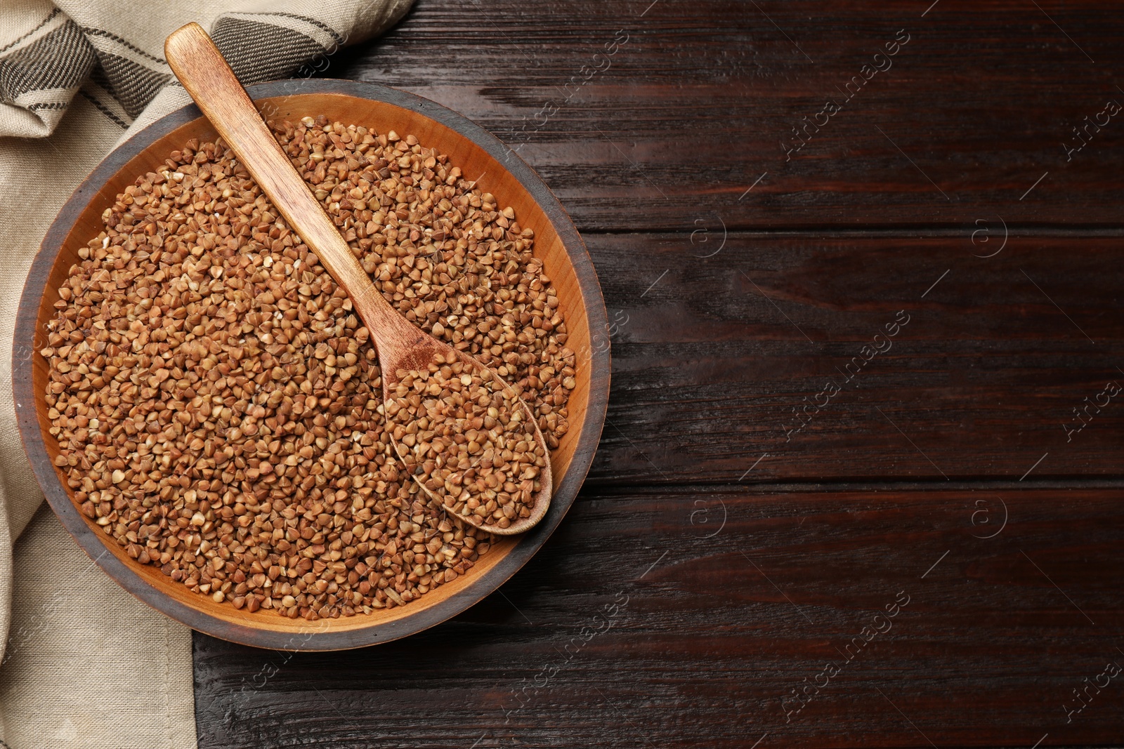 Photo of Bowl and spoon with dry buckwheat on wooden table, top view. Space for text