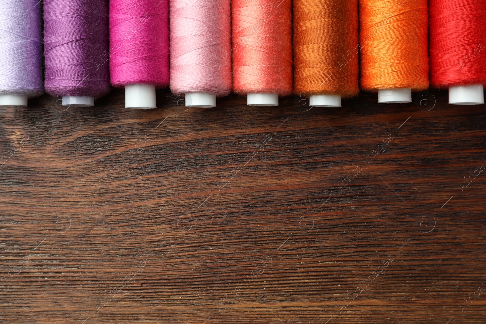 Photo of Set of colorful sewing threads on wooden table, flat lay. Space for text