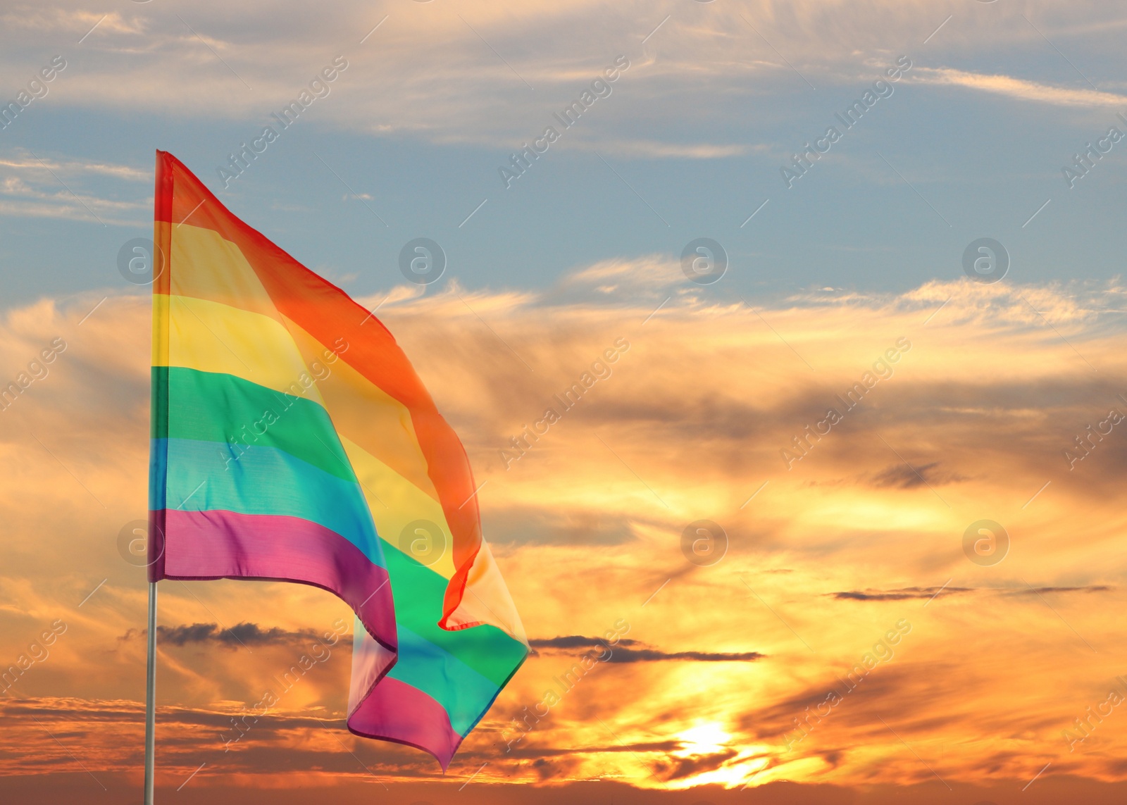 Image of Bright rainbow LGBT flag against sky at sunset