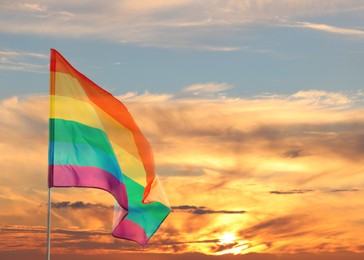 Bright rainbow LGBT flag against sky at sunset