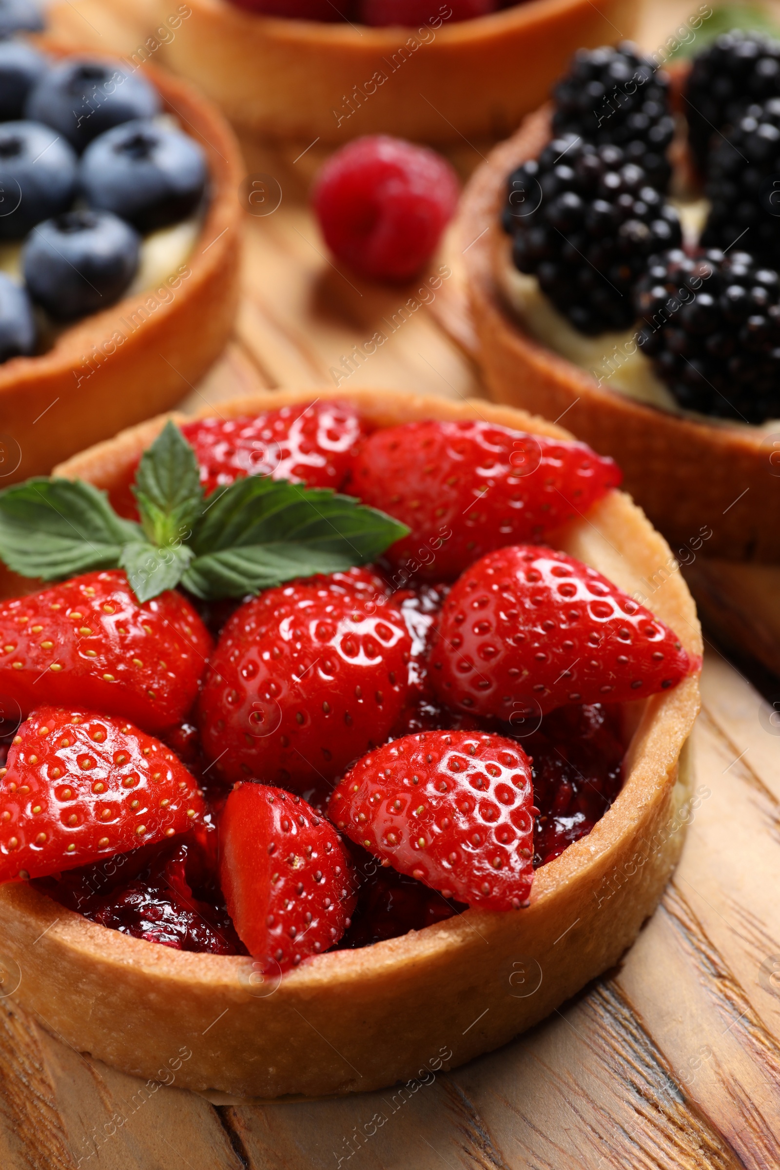 Photo of Tartlet with fresh strawberries on wooden table, closeup. Delicious dessert