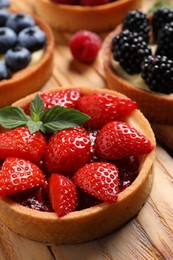 Photo of Tartlet with fresh strawberries on wooden table, closeup. Delicious dessert