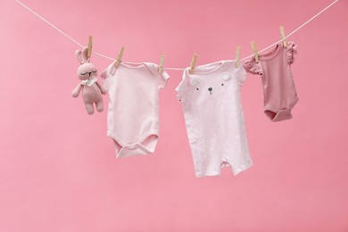 Different baby clothes and bunny toy drying on laundry line against pink background