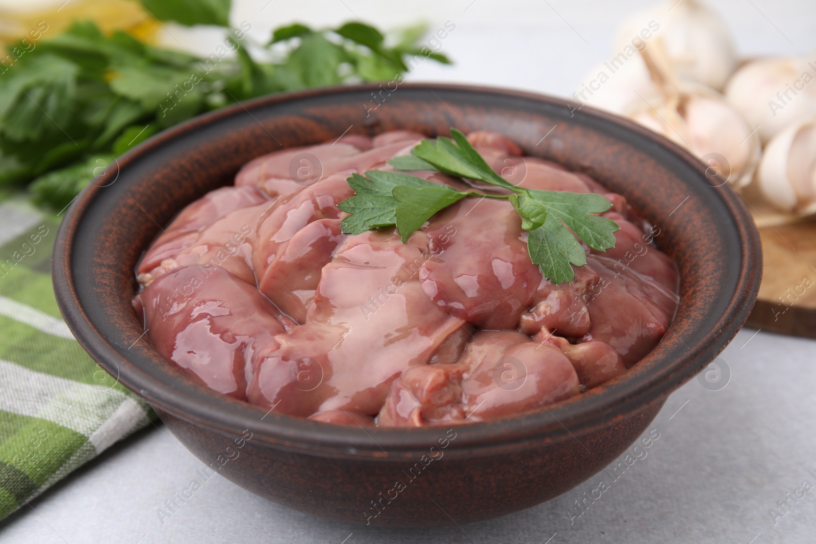 Photo of Bowl with raw chicken liver and parsley on white table