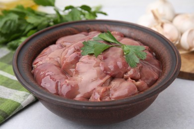 Photo of Bowl with raw chicken liver and parsley on white table