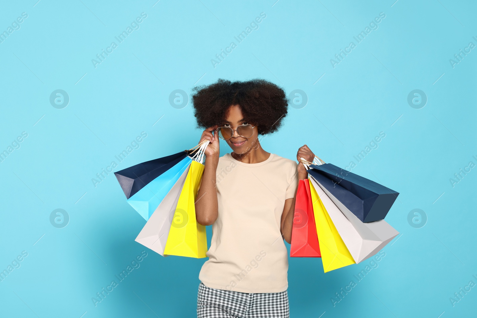 Photo of Happy African American woman in sunglasses with shopping bags on light blue background