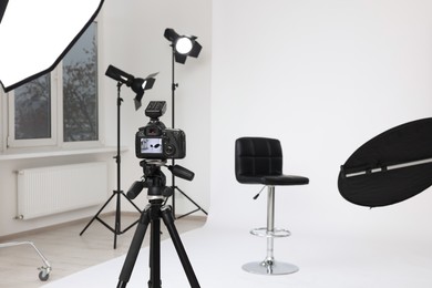 Photo of Camera on tripod, bar stool and professional lighting equipment in modern photo studio