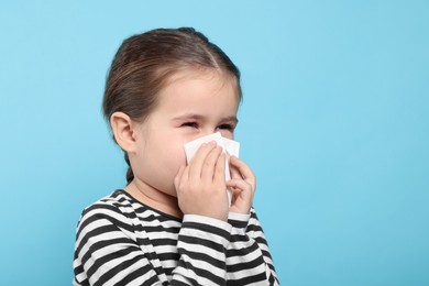 Girl blowing nose in tissue on light blue background, space for text. Cold symptoms