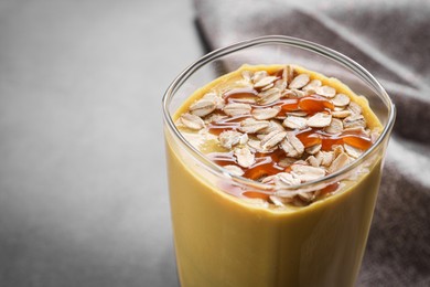 Photo of Glass of delicious smoothie with oat flakes and caramel syrup on grey table, closeup. Space for text