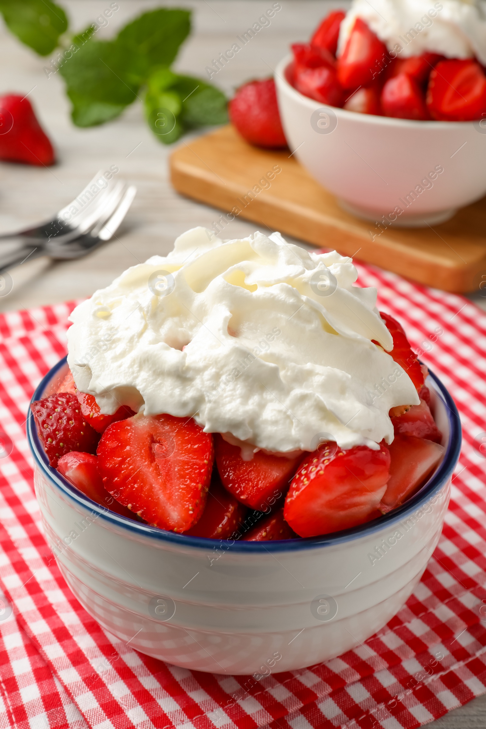 Photo of Bowl with delicious strawberries and whipped cream served on table, closeup