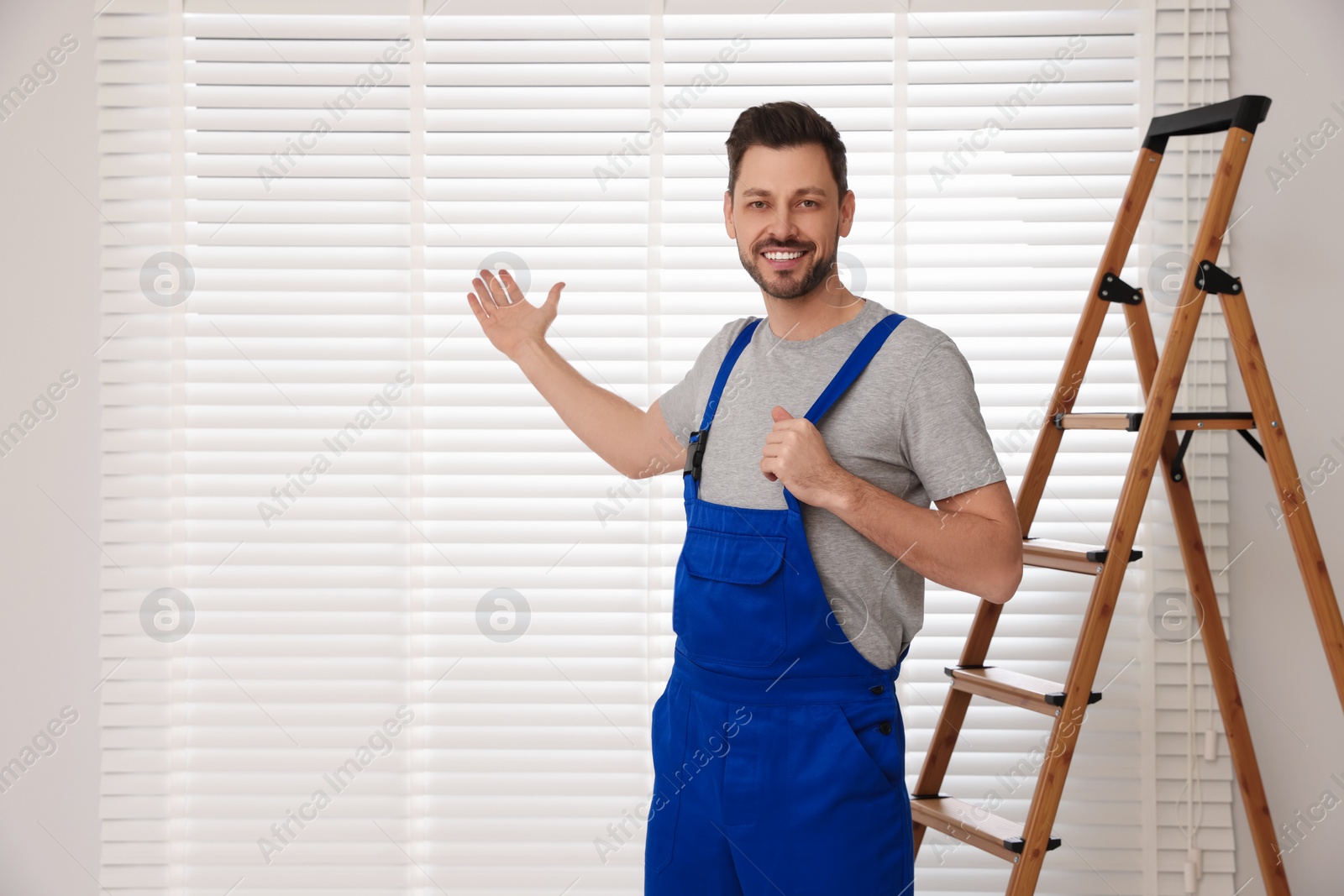 Photo of Worker in uniform and stepladder near horizontal window blinds indoors