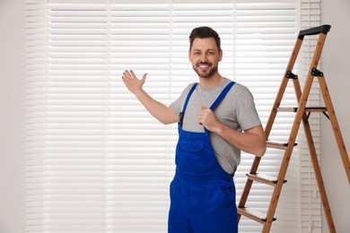 Photo of Worker in uniform and stepladder near horizontal window blinds indoors