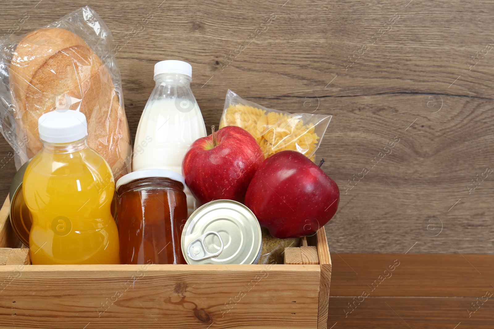 Photo of Humanitarian aid. Different food products for donation in crate on wooden table, closeup