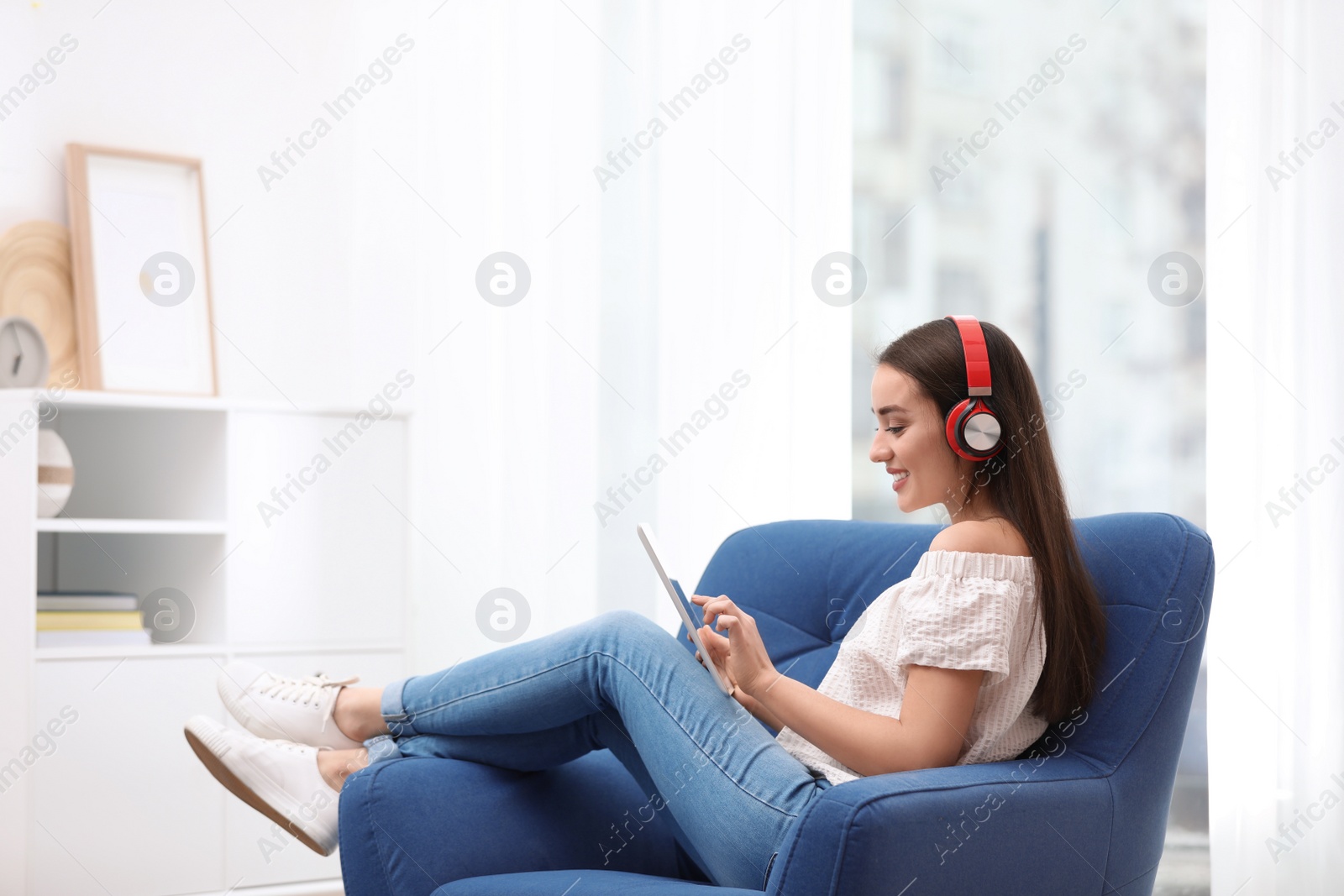 Photo of Young woman with headphones and tablet sitting in armchair at home